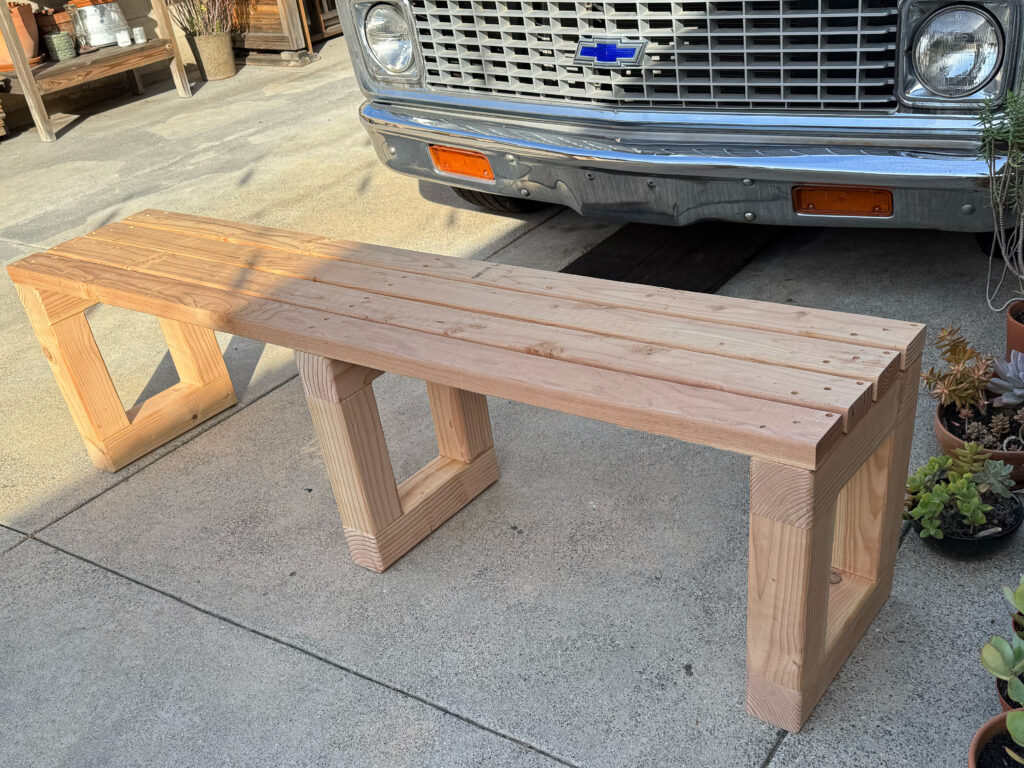 Handmade 2x4 bench photographed in a garage driveway with classic Chevy truck and workshop in background.